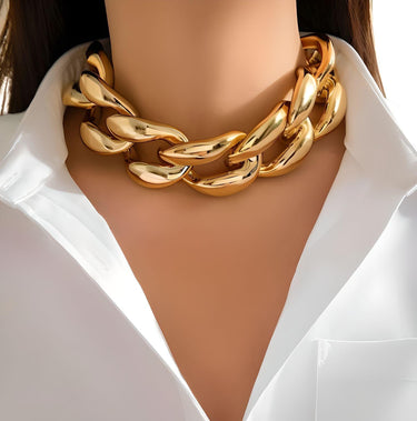 A woman wearing a white shirt and a thick gold chain choker necklace.